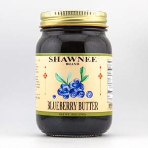 A jar labeled "Shawnee Brand Blueberry Butter" with a gold lid, featuring a blueberry illustration, against a plain white background.