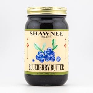 A jar of Shawnee Brand Blueberry Butter with a gold lid, featuring a label adorned with blueberry illustrations and product details.