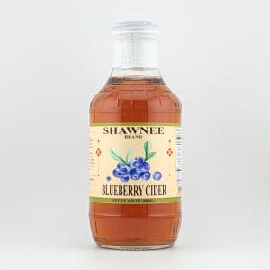 A small bottle labeled "Shawnee Brand Blueberry Cider" is filled with amber liquid. It features blueberry imagery and a white cap.