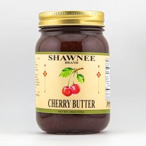 A jar of Shawnee Brand cherry butter with a golden lid and a label featuring cherries and decorative patterns against a cream background.