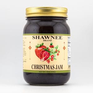 A jar of Shawnee Brand Christmas Jam with a gold lid, featuring strawberry and berry illustrations on its label, against a plain background.