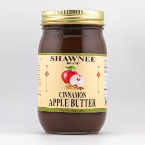 A jar of Shawnee Brand cinnamon apple butter with a light brown label and gold lid, featuring an illustration of sliced apples and cinnamon sticks.