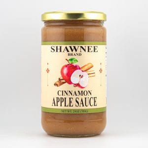 A 25oz jar of Shawnee Brand cinnamon apple sauce with a beige label, displaying red apples and cinnamon sticks, sealed with a gold lid.