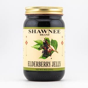 A jar of Shawnee Brand elderberry jelly with a gold lid, featuring a label displaying elderberries and leaves, against a plain background.