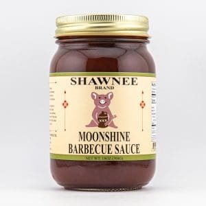 A jar of Shawnee brand Moonshine Barbecue Sauce with a humorous pig illustration. The label is light beige with decorative details and text.