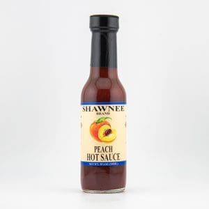 A bottle of Shawnee Brand Peach Hot Sauce with a yellow label and black cap, featuring a peach illustration on the front.