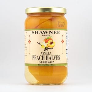 A jar of Shawnee Brand Vanilla Peach Halves in light syrup, featuring a decorative label with peaches and vanilla illustration. Net weight: 17 oz.