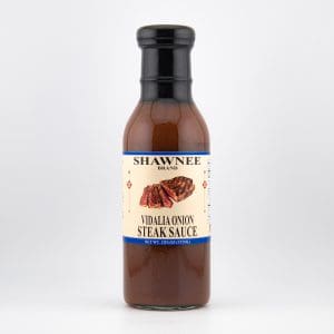 A bottle of Shawnee Brand Vidalia Onion Steak Sauce, featuring an illustration of steak on the label against a plain, light-colored background.