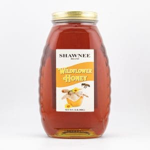 A jar of Shawnee brand wildflower honey with a gold lid displays a label featuring a honeycomb and bee design.
