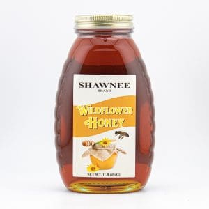 A 1-pound bottle of Shawnee Brand Wildflower Honey with a label featuring honey drizzling from a dipper and a bee near flowers.