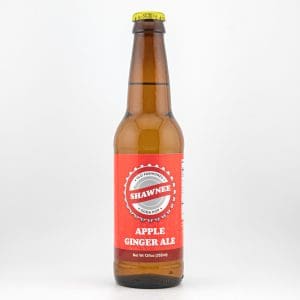 A glass bottle labeled "Shawnee Apple Ginger Ale" with a red label and yellow cap, standing against a plain white background.