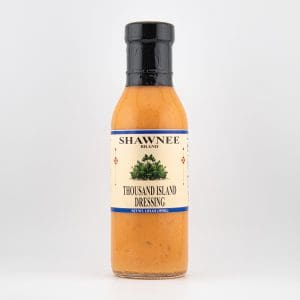 A bottle of Shawnee brand Thousand Island dressing, featuring a beige label with blue trim and green imagery, stands against a plain white background.