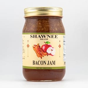 A jar of Shawnee Brand Bacon Jam with a gold lid, featuring bacon and apple illustration on the label, set against a plain background.