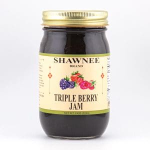 A glass jar with a golden lid labeled "Shawnee Brand Triple Berry Jam," featuring images of blackberries, raspberries, and strawberries on the front.