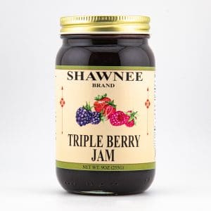 A jar of Shawnee Brand Triple Berry Jam with a label featuring images of blackberries, raspberries, and strawberries. Gold lid completes the design.