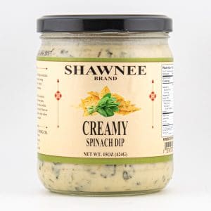 A jar of Shawnee Brand creamy spinach dip with a black lid, featuring green spinach and cheese on a beige label, weighing 15 ounces.
