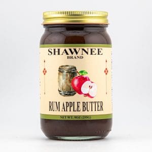 A jar of Shawnee Brand Rum Apple Butter featuring an illustration of apples and a barrel, with a gold lid and beige label.