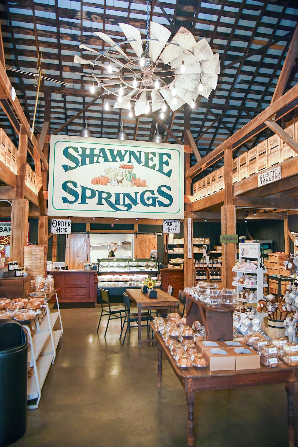 Interior of a rustic market named Shawnee Springs, featuring wooden beams, various products, a pastry section, and a vintage windmill chandelier.