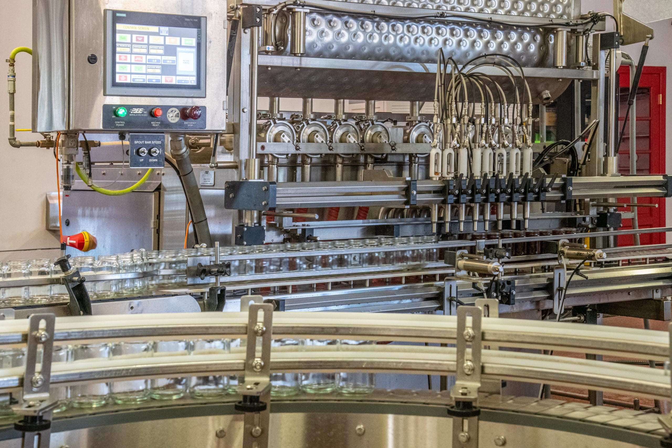 An industrial bottling machine with a control panel and conveyor system, designed for automated liquid filling in a manufacturing setting.
